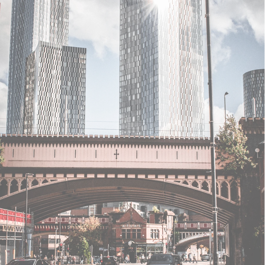 A brick railway viaduct in Manchester with modern towers rising behind it.