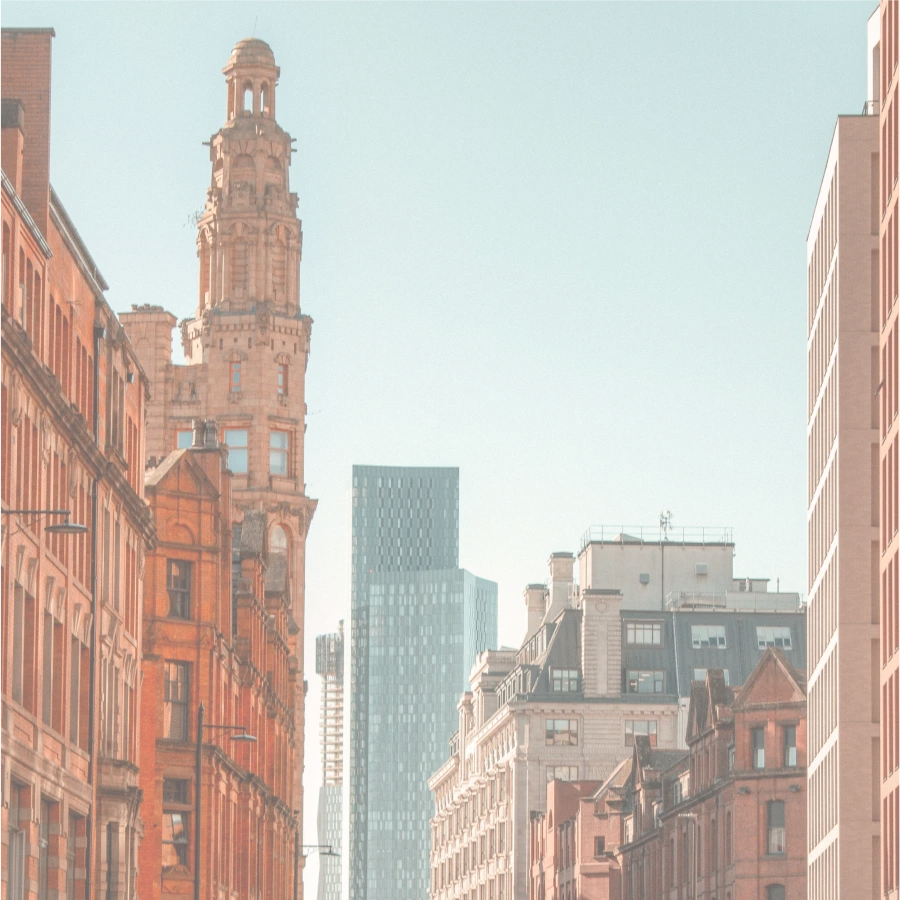 A red-brick Victorian building on a Manchester street, with glass towers behind.